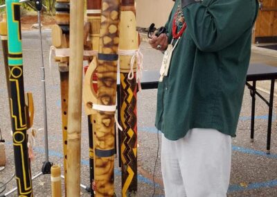 A man with a green headband sings into a microphone beside decorated wooden poles.