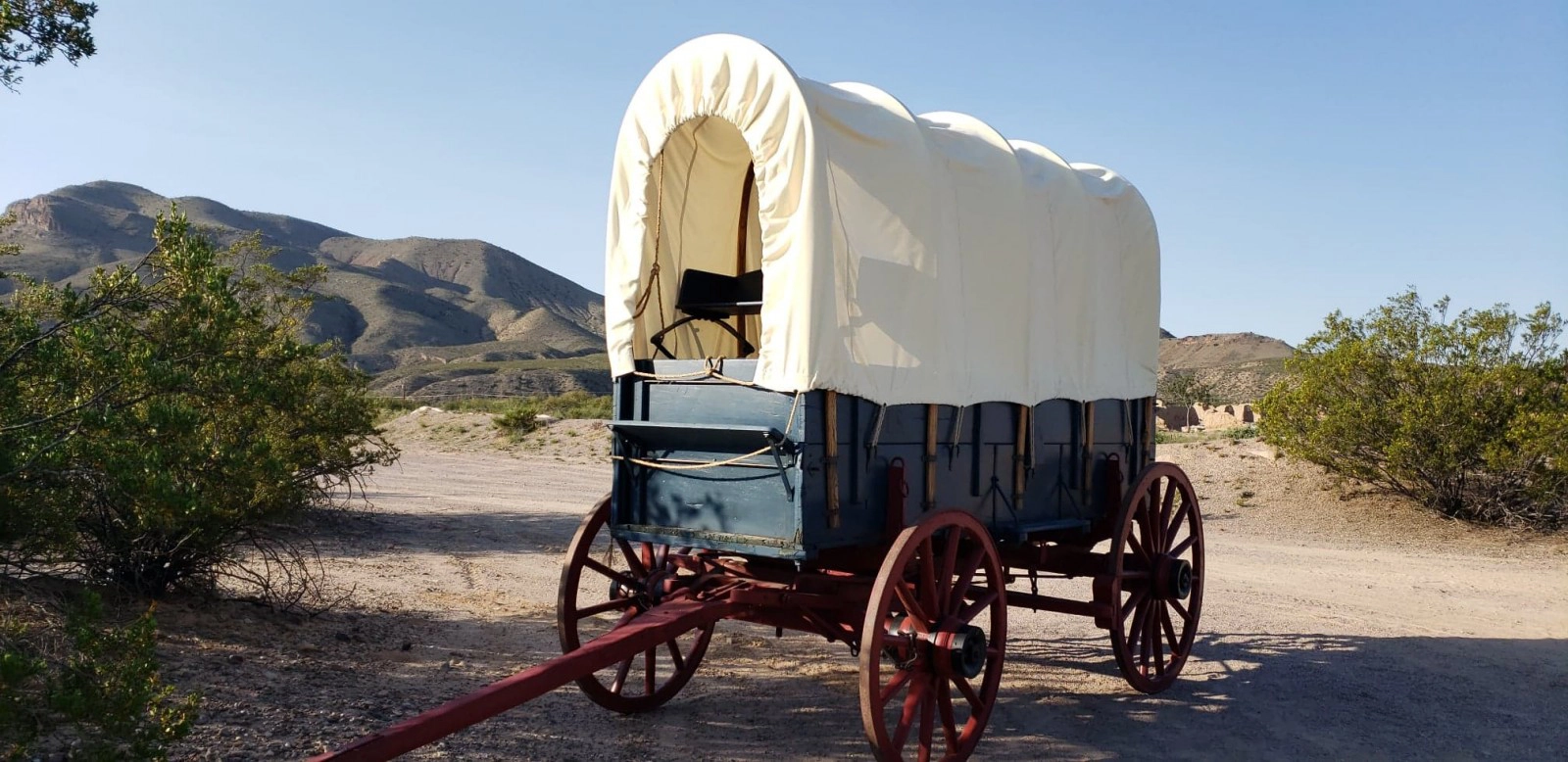 A canvas-topped covered wagon with a blue wooden body and red spoked wheels at Fort Selden Historic Site