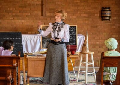 Teacher in Victorian-era dress lecturing to students in a vintage classroom.