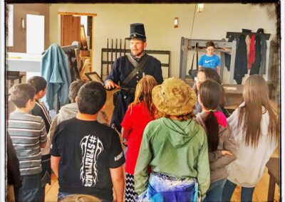 Man in top hat speaks to a group of children in a classroom setting.