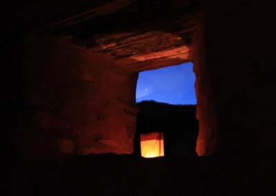 Dark interior with a glowing orange lantern seen through a doorway, blue sky beyond.