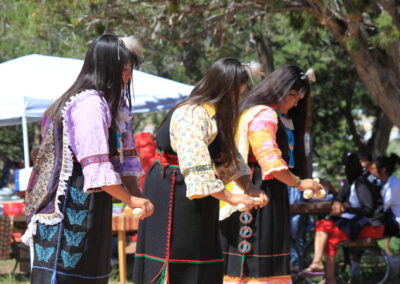 Three women in colorful traditional outfits performing outdoors.