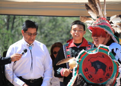 Outdoor scene with a group of people, one wearing a feathered headdress and holding a drum.