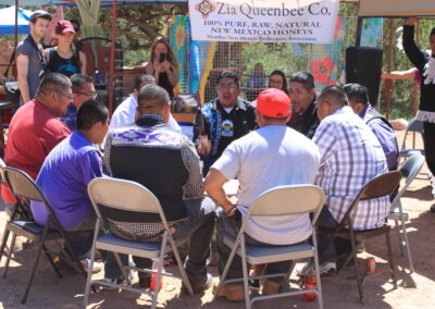 Community meeting outdoors with people seated in folding chairs in a circle under a tent.