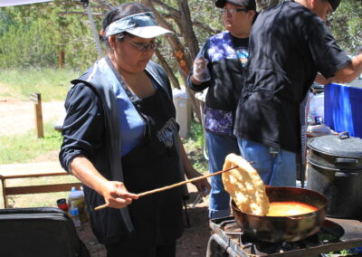 Outdoor cooking scene with a woman stirring a pot over a camp stove.