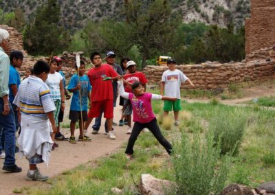 Group of people watching a person in pink jump outdoors near ruins.