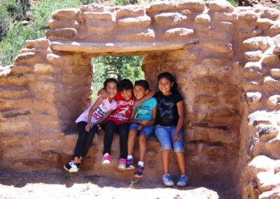 Four kids sit on a mud-brick bench in a rustic doorway, smiling.