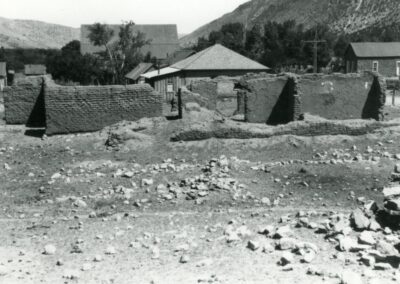 Dusty village with small pyramid-shaped huts and a rocky hillside in the background.