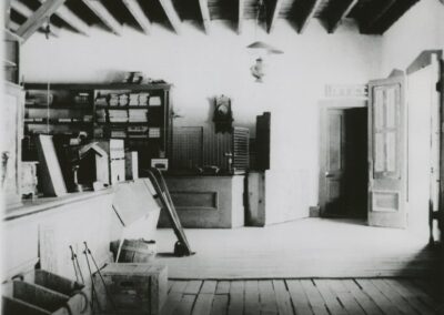 Old attic workshop with wooden beams, workbench, shelves, and an open doorway.