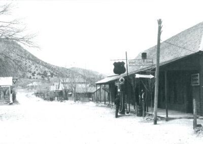 Old village street with thatched huts and villagers beside a signpost.