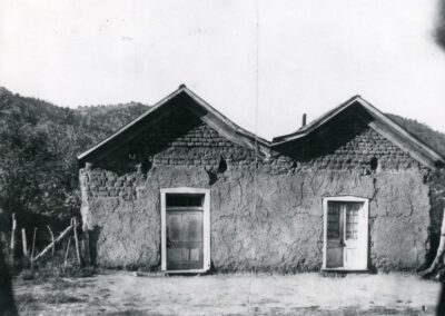Rural adobe house with a door and window beneath a pitched roof.