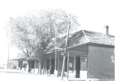 Old storefront on a quiet street with trees and utility poles.