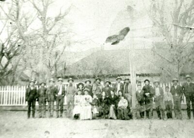 Group of people in vintage clothing posing outdoors near a white fence.