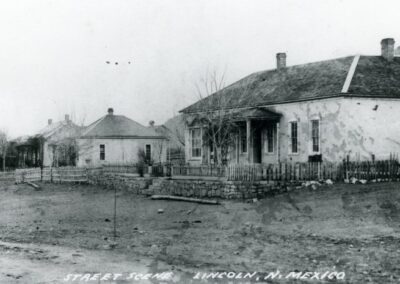 Thatched-roof cottages and fences along a dirt road in a rural scene.