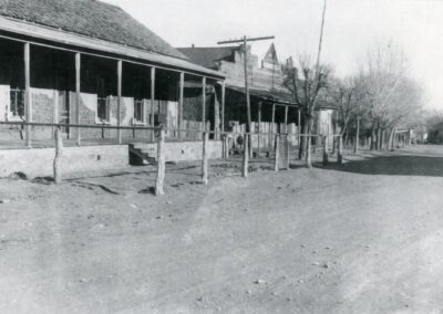 A historic street scene with a porch-lined building and dirt road.