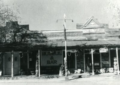 Old street with a row of storefronts and a bar, with pedestrians on the sidewalk.