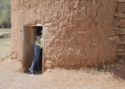 Person in a yellow shirt stands in the doorway of a round mud-brick building.