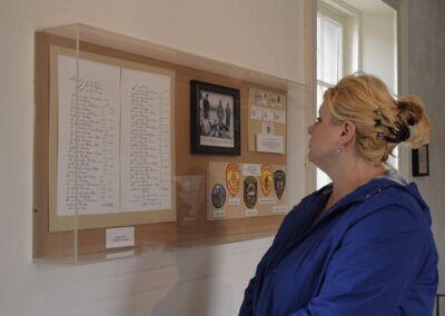 Woman in a blue jacket studies a wall display of documents, photos, and badges.