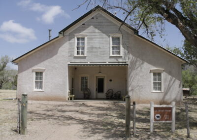 White two-story house with a front porch, dirt yard, and a tree on the right.