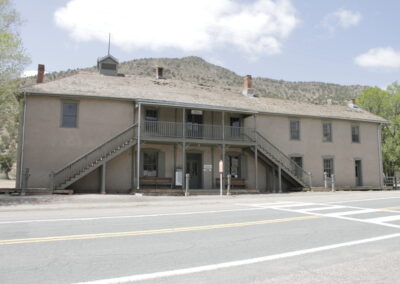 Two-story beige building with exterior stairs and a balcony, beside a road.