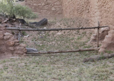 Old wooden log fence across a dry yard with stone walls.
