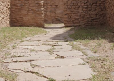 Stone-paved path through ancient ruins with brick walls and grassy ground.