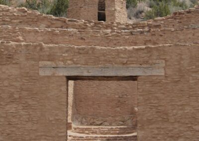 Ancient mud-brick ruin with doorway and steps against a hillside.