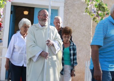 Priest in white robes leads a church ceremony at the entrance under a floral arch.