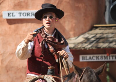 Cowboy in vest and hat holding a rope in a western town.