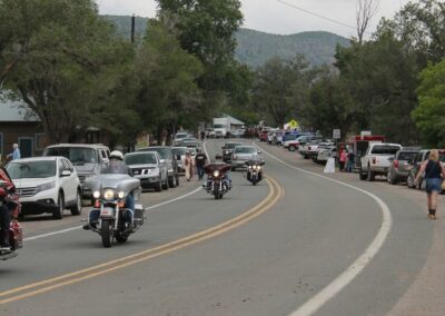 Curving road with cars and motorcycles, trees, and hills under an overcast sky.
