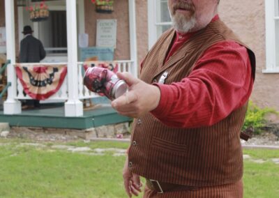 Man in cowboy attire points a pistol outdoors in front of a house.
