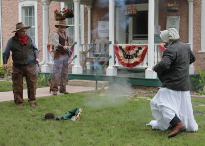 Living history reenactors an outdoor gunfight scene in front of a Victorian-style building