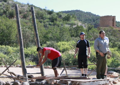 Three men build a wooden frame outdoors in a rural, hilly area.
