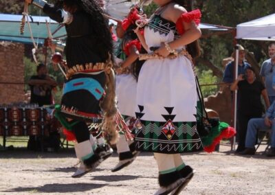Two dancers in colorful traditional regalia perform a dance outdoors.