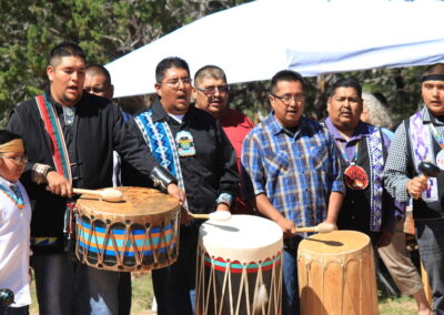 Group of men in traditional attire playing drums outdoors.