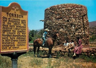 Historic circular stone tower with a nearby sign and people on horseback.