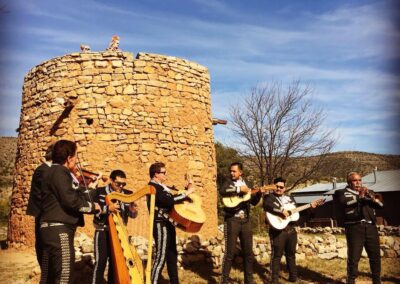 Group of musicians playing string instruments outdoors beside a stone tower.