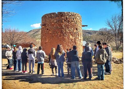 A group of people stands around a circular stone tower in a desert landscape.