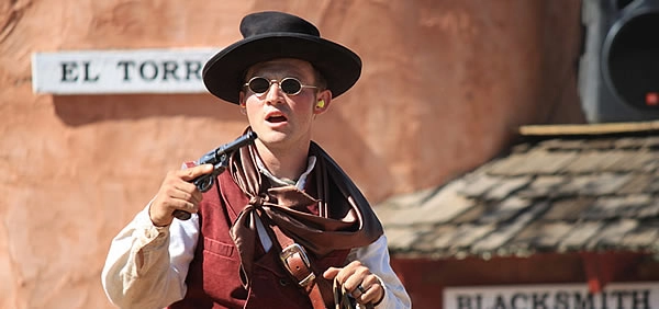lincoln-outlaw A living history reenactor in frontier-era clothing holds a revolver during an outdoor performance
