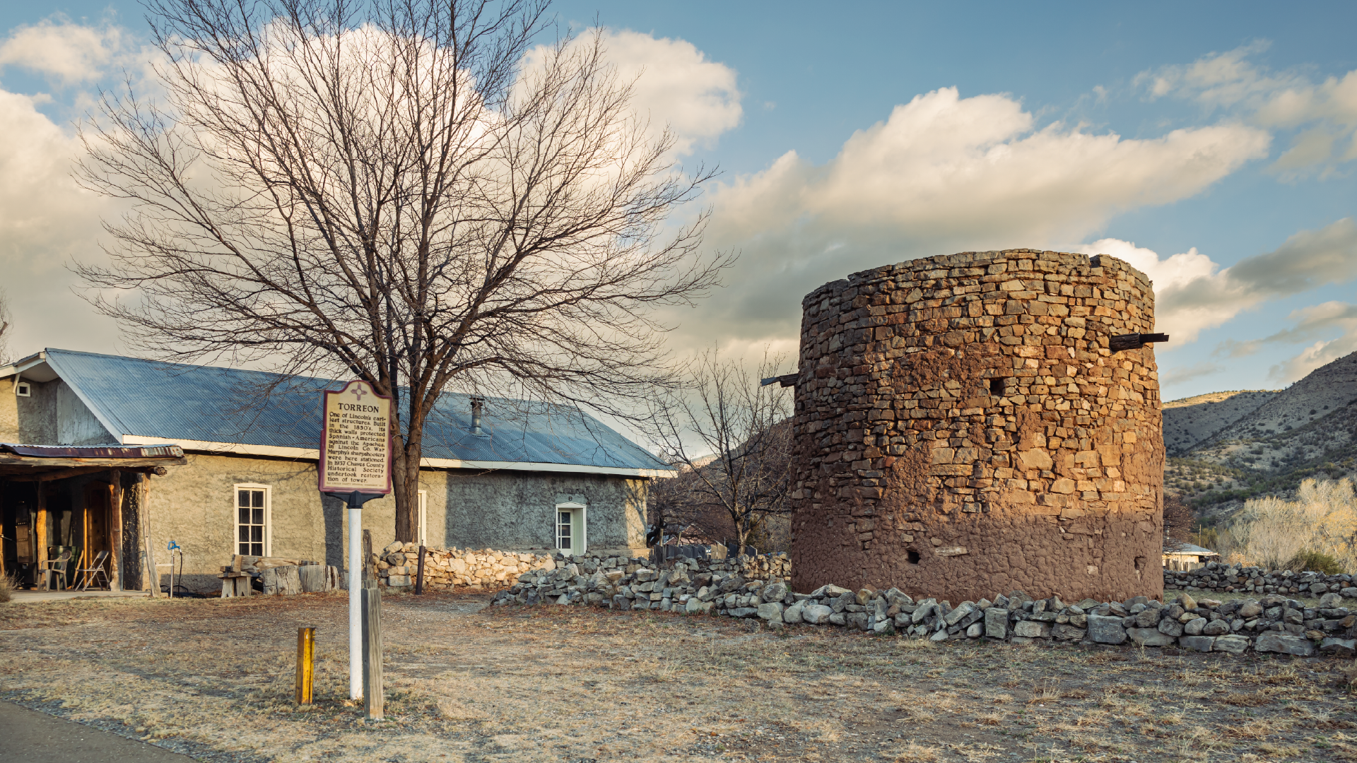 Round adobe tower next to a historic marker and old house
